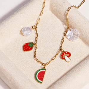 Gold titanium steel necklace with fruit charms and pearls on a beige jewelry display tray