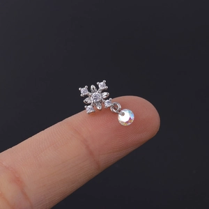 Macro shot of a tiny silver snowflake stud earring with rainbow bead on a fingertip