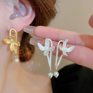 Close-up of matte metal flower earrings with white pearl drop in gold and silver finish