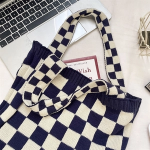 Close-up of knit checkerboard tote bag in navy and beige with laptop and books