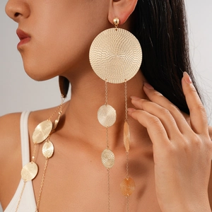 Detail of long gold tassel earrings with textured round disks worn by a model