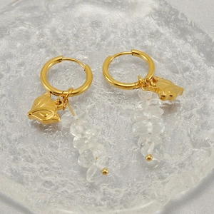 Detail of gold fox pendant earrings with natural white crystal stones on a glass plate
