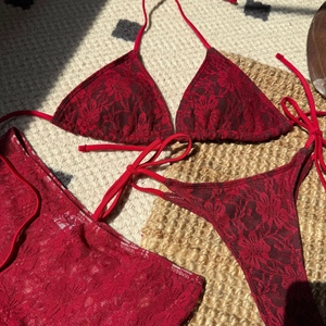 Bikini trois pièces en dentelle rouge avec paréo floral posé sur un tapis tressé