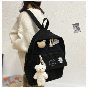 Detalle de mochila de pana negra con colgante de oso y pines en modelo femenino