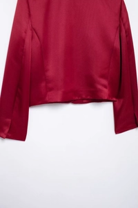 Close-up of the red satin long-sleeve top showing smooth fabric texture and hem detail