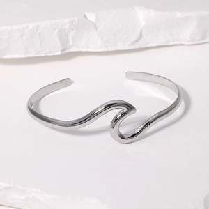 Macro shot of wave-shaped silver stainless steel open bangle on a textured white pedestal