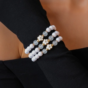 Close-up of three-piece acrylic beaded bracelets with white flower charms on a model's wrist