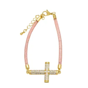 Detalle de una pulsera de cruz chapada en oro con circonitas blancas y cordón de malla rosa