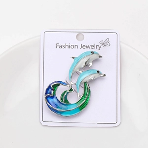Detail of dolphin brooch with blue and white enamel jumping over waves on a card