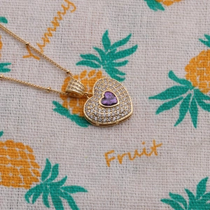 Macro detail of heart pendant necklace with purple center stone and gold chain