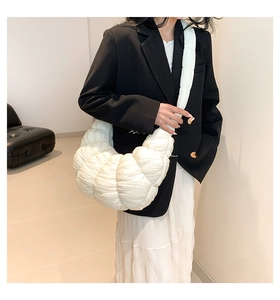 Close-up of white crescent bag with quilted pleated texture and wide shoulder strap