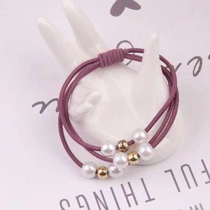 Détail d'un élastique à cheveux triple brin violet foncé avec perles sur présentoir main