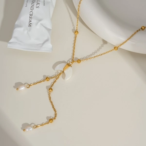 Golden crescent moon necklace with white jade and pearl pendant on a minimal display