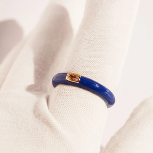 Adjustable blue enamel ring with a rectangular gold-rimmed zircon stone on a gloved finger