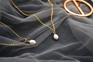 Close-up of elegant gold chain necklace featuring white teardrop pearl pendants on mesh background