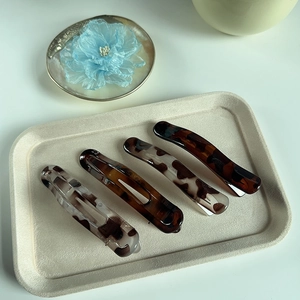 Set of four tortoiseshell acetate hair clips displayed on a textured aesthetic tray