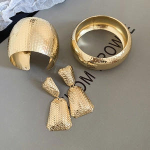 Close-up of golden jewelry set with hammered texture bracelets and woven earrings