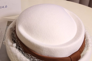 Close-up of white wool pillbox hat with elegant mesh veil and brown satin ribbon trim