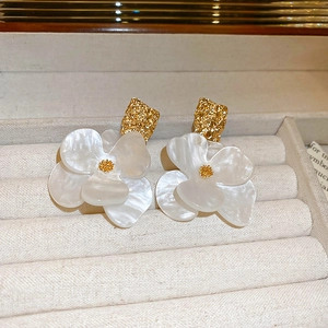 Close-up of white acrylic flower earrings with golden texture on a beige velvet tray
