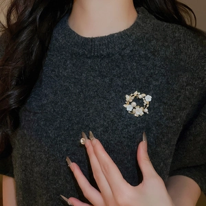 Detail of flower brooch with 18k gold plating, pearls and zircons on grey sweater