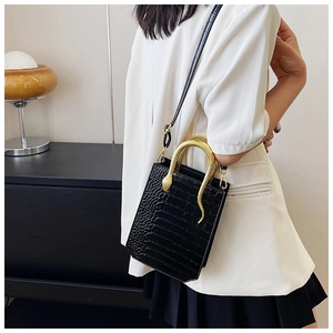 Detail of small black tote bag featuring crocodile pattern and gold snake-shaped handle