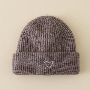 Detailed close-up of dark brown knit beanie with white hand-drawn heart embroidery