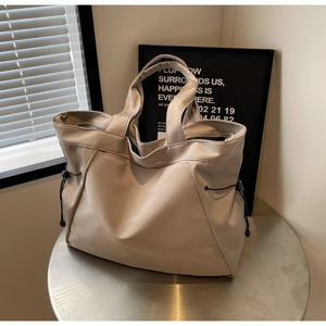 Detail view of large beige nylon tote bag featuring adjustable black side drawstrings