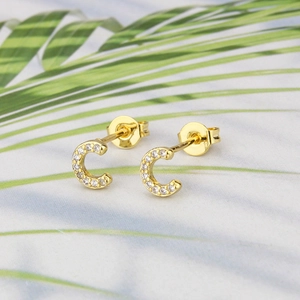 Close-up of gold-plated C-letter stud earrings with zircon inlays on palm leaf
