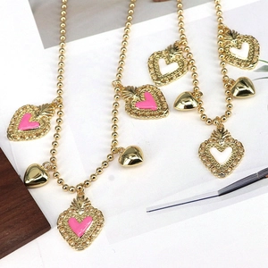 Detail of gold beaded necklaces with pink and white enamel heart pendants on white paper