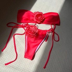 Detailed view of pink bikini featuring 3D satin rose applique on bandeau top and side-tie bottoms