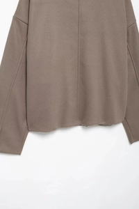 Detail view of the thick wool blend fabric texture and stitching on the brown coat's hem