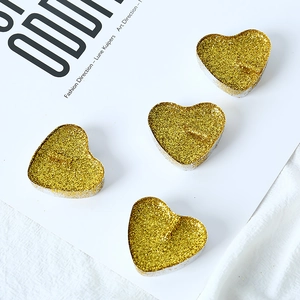 Close-up of four heart-shaped golden glitter tealight candles with sparkling texture