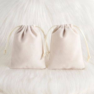 Detail of two beige plush velvet drawstring pouches for jewelry on white fur texture