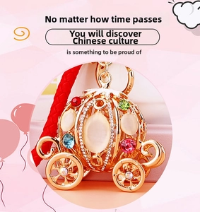 Detail of a golden pumpkin carriage keychain featuring colorful rhinestones and red cord