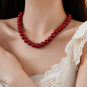 Detail of a deep red round beaded necklace worn against a white lace blouse