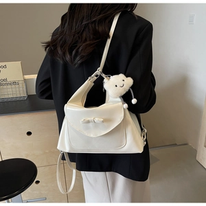 Detail of minimalist cream tote bag with bow accent and plush cloud charm on shoulder strap