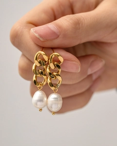 Close-up of gold Cuban chain earrings with white baroque pearl pendants worn by a model