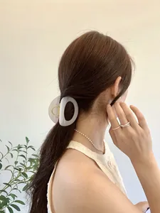 Detail showing a translucent grey oval hair claw clip with pearl necklace and silver rings