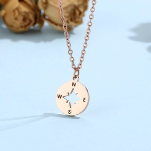 Détail d'un collier boussole en or rose avec étoile évidée et gravure directionnelle WNES