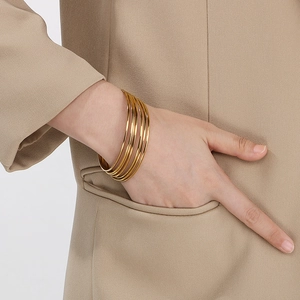 Detail view of stacking 18K gold plated titanium bangles on a model wearing a blazer