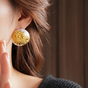 Close-up of vintage gold chrysanthemum stud earrings with white circular enamel base