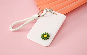 Close-up of a white plastic card holder with green daisy charm and braided wristlet strap