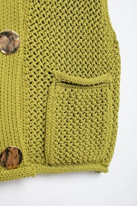 Detailed close-up of green knit vest texture featuring gold metal buttons and pocket