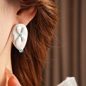Detailed close-up of a silver floral earring with turquoise beads on a female model