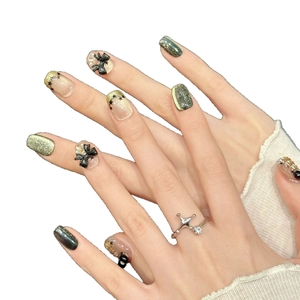 Press-on nails with champagne gold glitter, black stars and 3D bows on white background