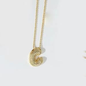 Close-up of a gold 'C' letter pendant with sparkling crystals on a fine chain