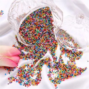 Colorful 2mm glass seed beads pouring from a glass jar onto white silk fabric background