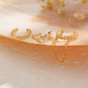 Detalle de set de tres ear cuffs dorados con circonitas y cadena sobre una caracola