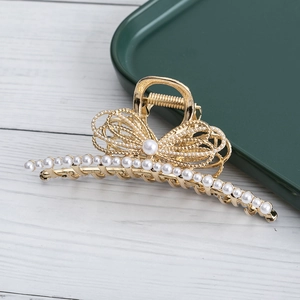 Detailed view of a golden metal hair claw clip featuring pearls and a bow-knot decoration