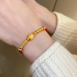 Détail d'un pendentif poisson en or et de perles sur un bracelet en corde tressée rouge